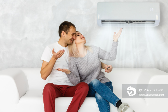 Smiling Young Couple Sitting On Sofa Using Air Conditioner