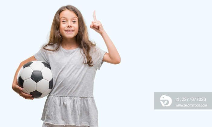 Brunette hispanic girl holding soccer football ball surprised with an idea or question pointing finger with happy face, number one