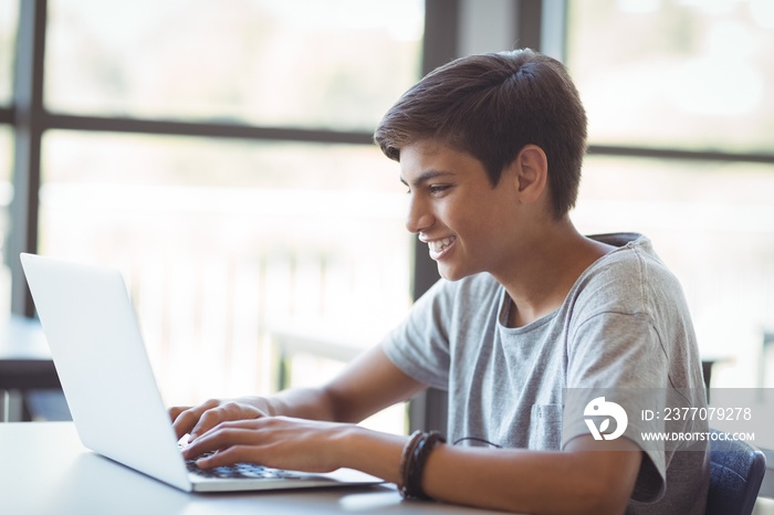 Happy schoolboy using laptop in classroom