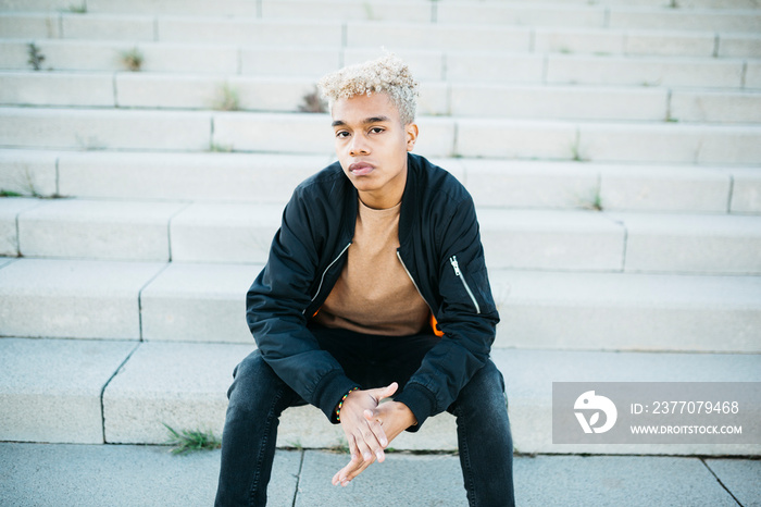 Young latin american male sitting on stairs at the street