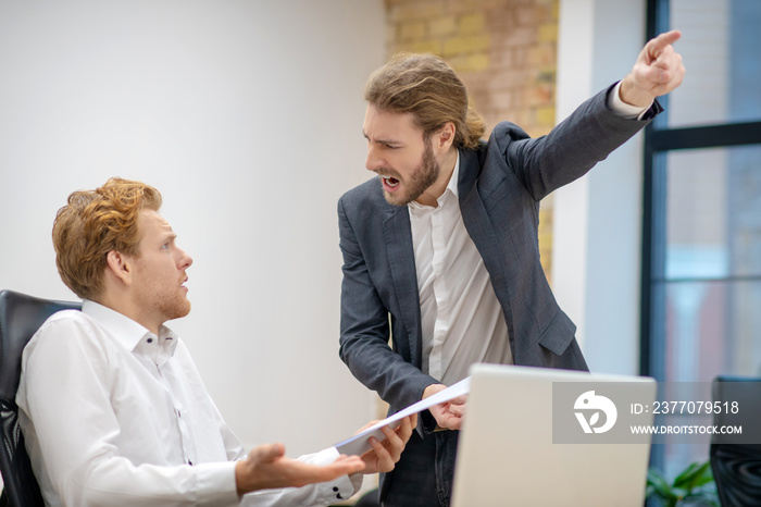 Screaming man pointing with hand and bewildered colleague