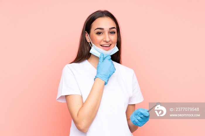 Woman dentist holding tools isolated on pink background laughing