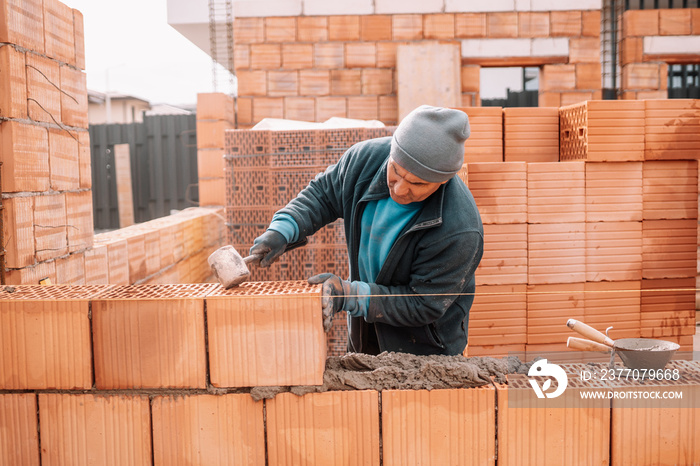 Bricklayer industrial worker installing brick masonry on exterior wall with trowel putty knife and rubber hammer