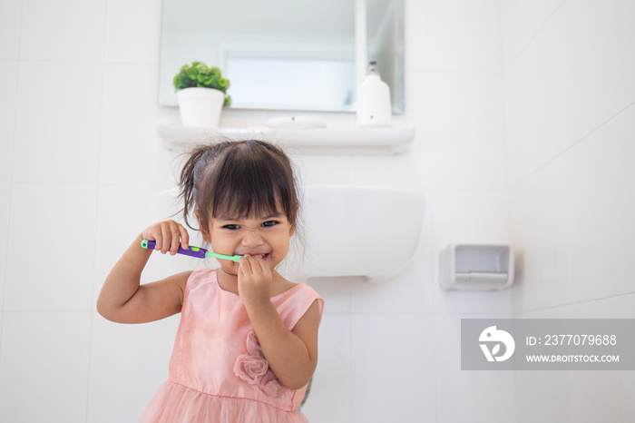 Little cute baby girl cleaning her teeth with toothbrush in the bathroom