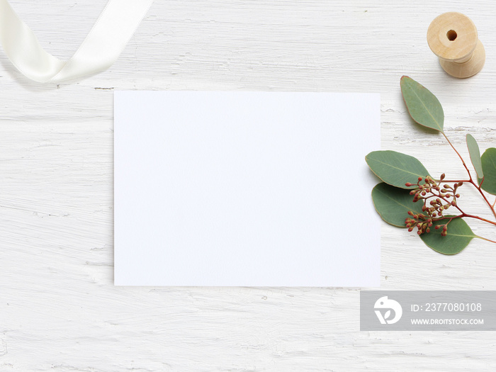 Feminine wedding desktop mock-up with blank paper card and Eucalyptus populus branch on white shabby table background. Empty space. Styled stock photo, web banner. Flat lay, top view.