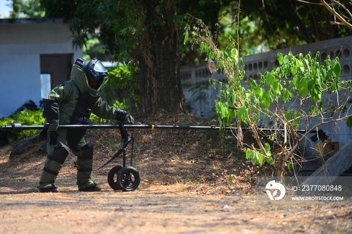 EOD officer in The explosive ordnance disposal suit using remote robot hand to check the unclear box beside the wall