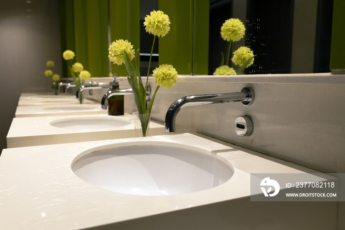 Closeup metal tap or faucet on white toilet sink. Clean restroom with basin and flower decoration.