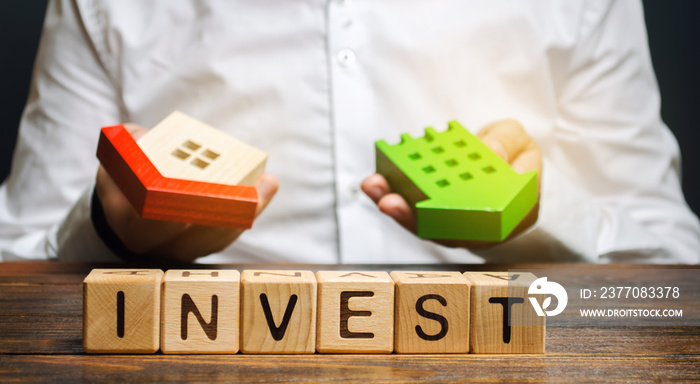 Wooden blocks with the word Invest and houses in the hands of a businessman. The concept of investing in real estate construction. Effective investment. Buying apartments. Business and finance