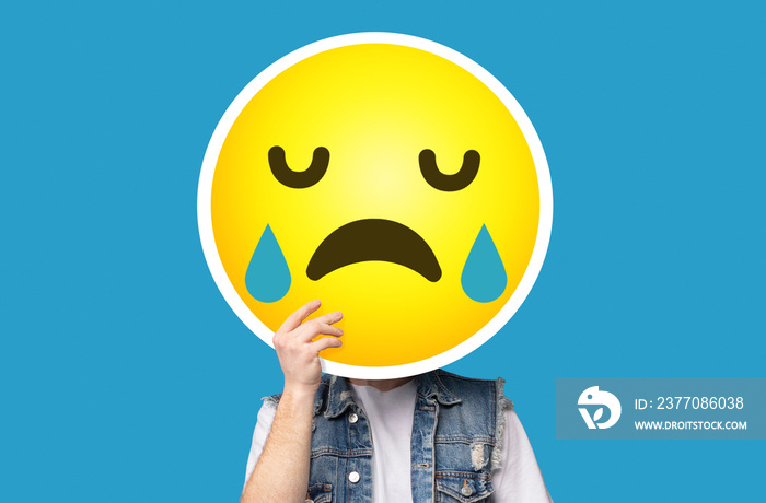 Unrecognizable man hiding his face behind crying sad emoticon emoji