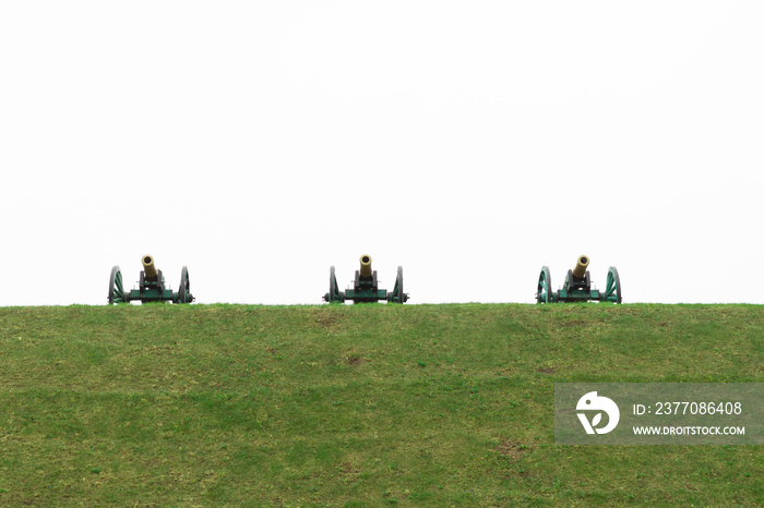 Old cannons, built in a redoubt on a hill. Old cannons stand on high ground, at a strategic height. Three old cannons stand on a hill against a white sky.