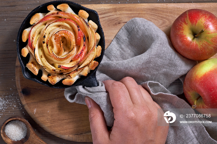 Hand holding omemade puff pastry with rose shaped apple slices baked in iron skillet