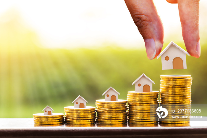 Woman hand hold a wooden home model put on the stack coin with growing in the public park, Savings money for buy house and loan to business investment for real estate concept.