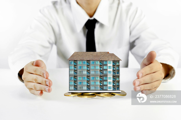 businessman hands protecting condominium model with piles of golden coins