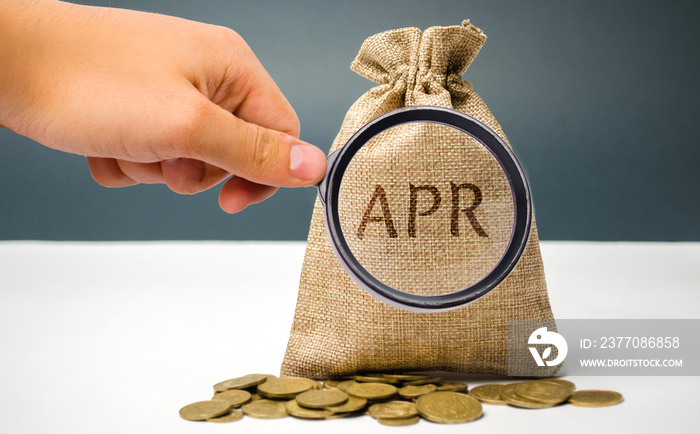 A hand points to a money bag with the word Apr. This is a financial fee, expressed as an annual rate. Applicable to loan, mortgage, credit card. Commercial money investment. APR. Percentage Rate