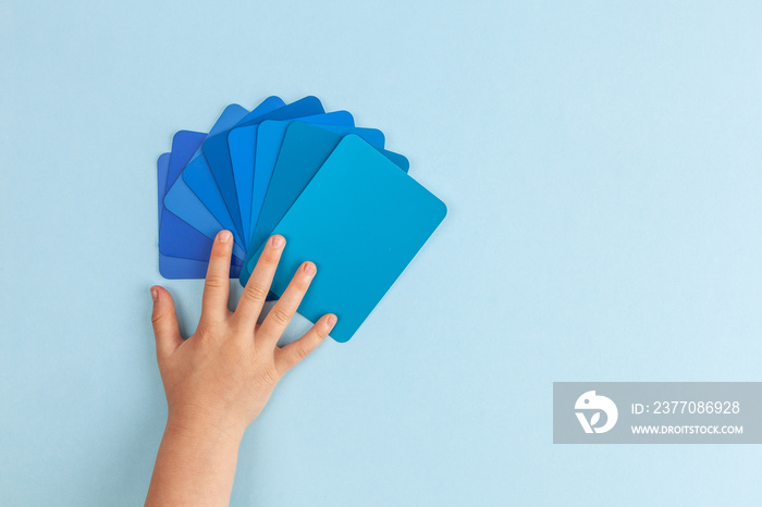 Child’s hand touching color samples cards - hues of blue. Top view with copy space