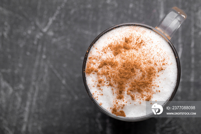 Top view of delicious cappuccino coffee with milk foam sprinkled with cinnamon in a transparent glass mug on a gray background, horizontal format