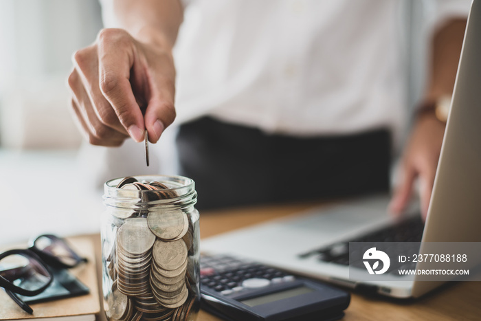 Businessman wearing white shirt working on desk office and hand holding coins putting in glass and calculating money to be invested in order to grow. Concept saving money for finance accounting.