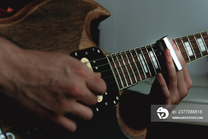 Person sliding a bottle neck along the strings of an electric guitar. Selective focus. Copy space.