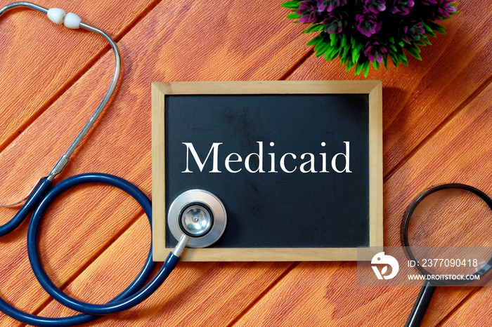 Top view of stethoscope,magnifying glass,plant and blackboard written with Medicaid on wooden background. Health concept.