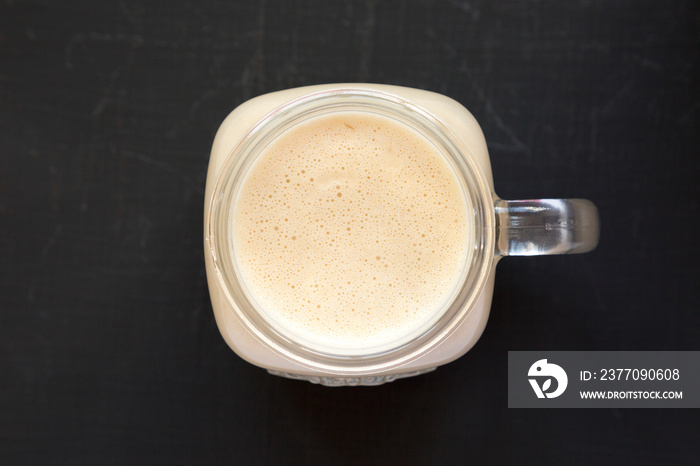 Peanut butter banana smoothie in a glass jar on a black surface, top view. Overhead, flat lay, from above. Close-up.