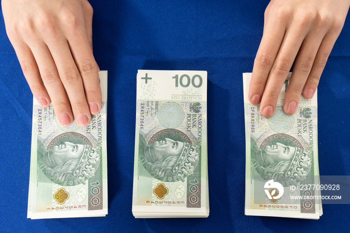 Three piles of banknotes stacked on the table with the hands of a young woman. A large sum of cash in one place.