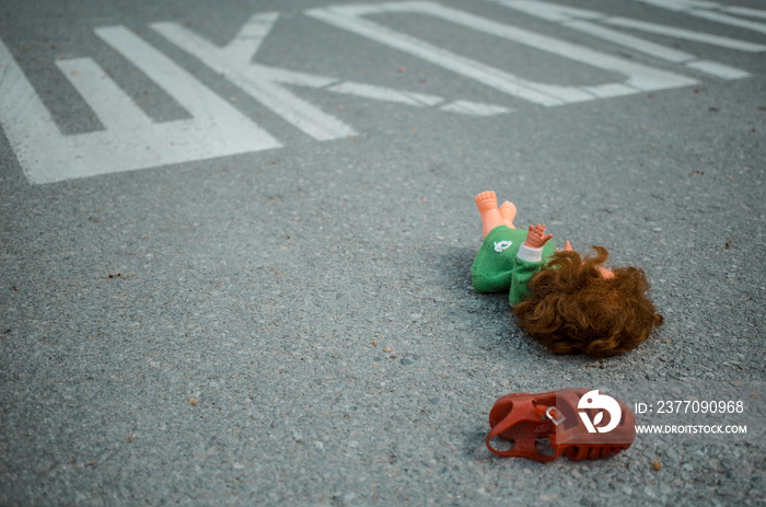 Old doll toy and red sandal in the middle of the road near school.