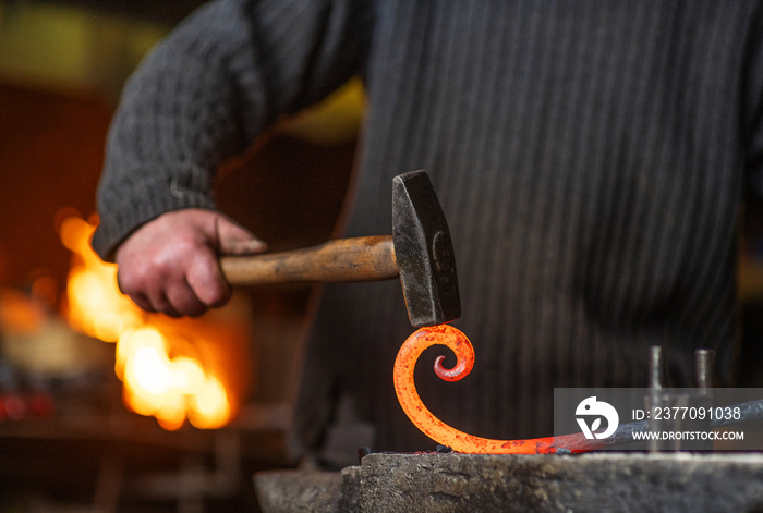 A close-up image of a blacksmith’s hands forging a spiral from a red-hot billet against the background of a forge. Handicraft concept