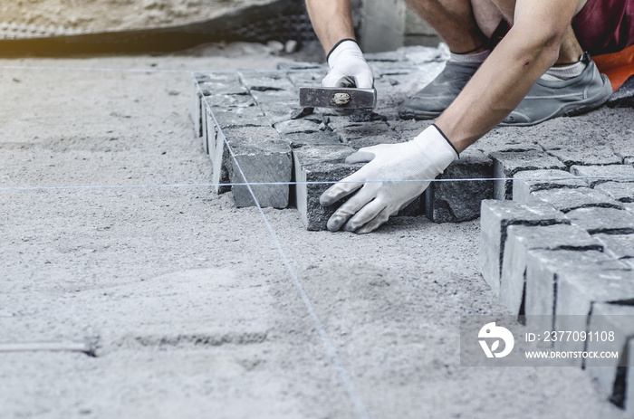 Worker lays gray granite pavement tiles on the marked site. Arrangement of urban environment. Repair of city roads