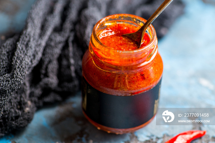 Red hot tomato sauce with chili pepper on the background of cans with sauce