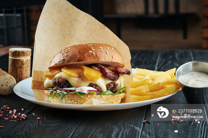 Appetizing and juicy burger with a large beef patty, melted cheddar cheese, arugula, onion, white sauce and peach on a white plate with french fries.