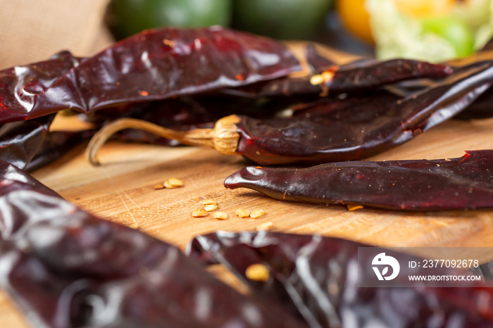 A closeup view of several dried California chili peppers on a wood cutting board.