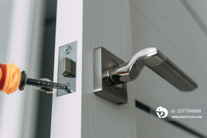 Repairing the door lock in the room using a screwdriver. The concept repair yourself. Close-up. Selective focus.