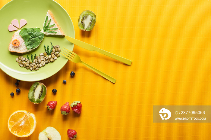 top view of plate with fancy fish made of food near fruits and cutlery on colorful orange background