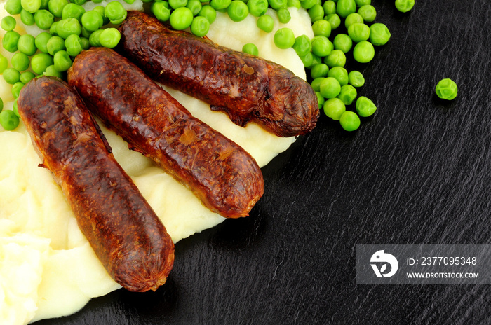 Sausages and mashed potato meal with garden peas on a slate background