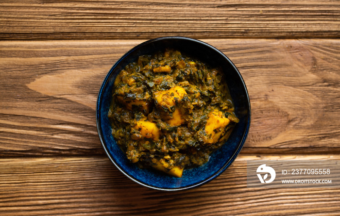 Indian Palak paneer on wooden rustic background. Traditional Indian dish with cheese paneer and spinach gravy. Healthy vegetarian meal. Top view.