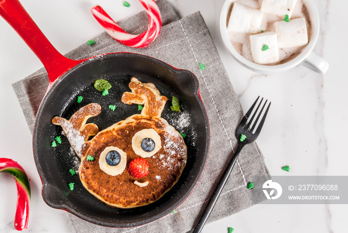 Funny food for Christmas. Kids breakfast pancake decorated like reindeer, with hot chocolate with marshmallow, white table copy space top view