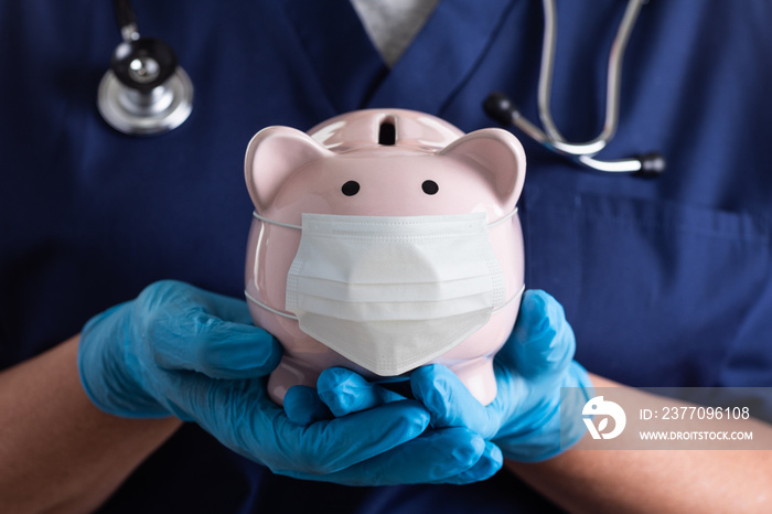 Doctor or Nurse Wearing Surgical Gloves Holding Piggy Bank Wearing Medical Face Mask