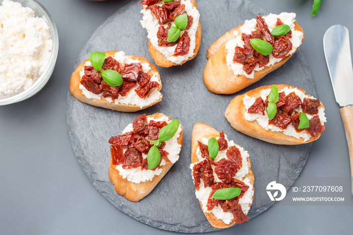 Bruschetta with sun dried tomato, feta and philadelphia cheese and basil on stone plate, horizontal, top view, closeup