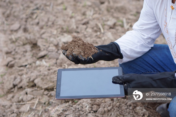 Hands holding smart tablet and soil. Concept about using digital wireless technology to research and collect data about agriculture problem. Checking soil quality before growing plants. Environment.