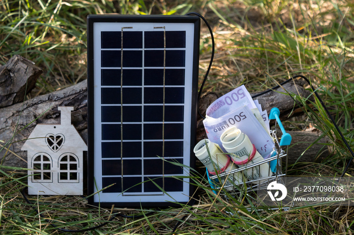 On the grass is a mock-up of a house, a solar panel and a supermarket trolley with money..