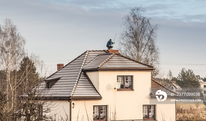 A chimney sweep cleans the chimney on the roof of a detached house