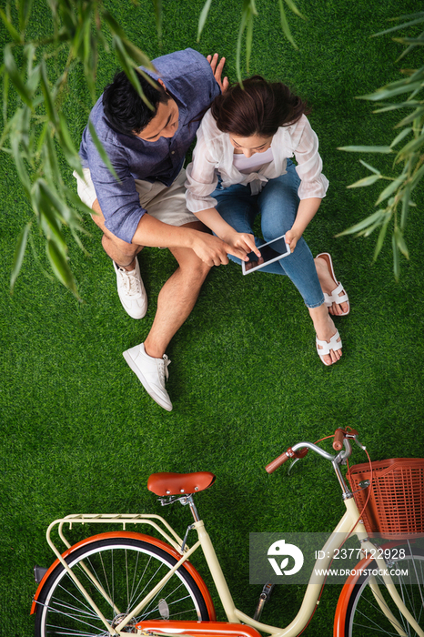 青年伴侣坐在草地上使用平板电脑