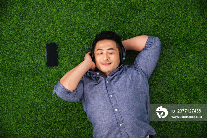 青年男人躺在草地上听音乐