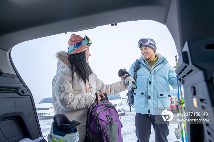 停车场内青年伴侣从汽车后备箱拿雪具