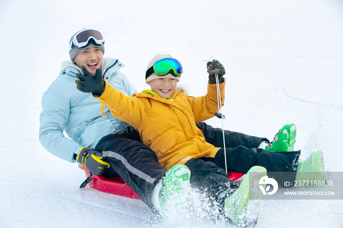 兴奋的父子坐着雪上滑板滑雪