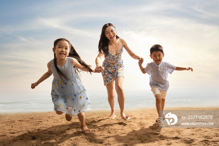 年轻母亲牵着两个孩子在沙滩上奔跑