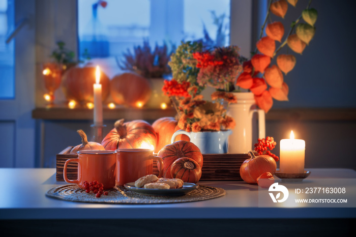 two orange cups  of tea and autumn decor with pumpkins, flowers and burning candles on table