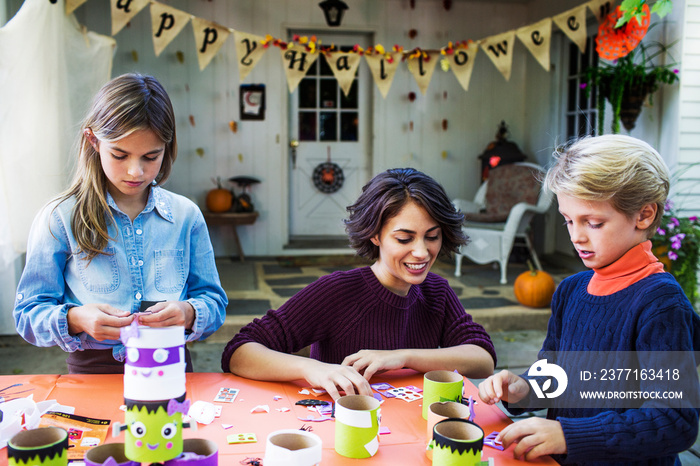 Happy mother assisting children while making decoration at table during Halloween party