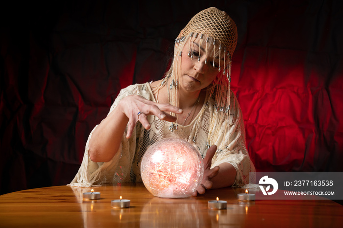 Fortune Teller with Crystal Ball on table with candles and black and red mottled background