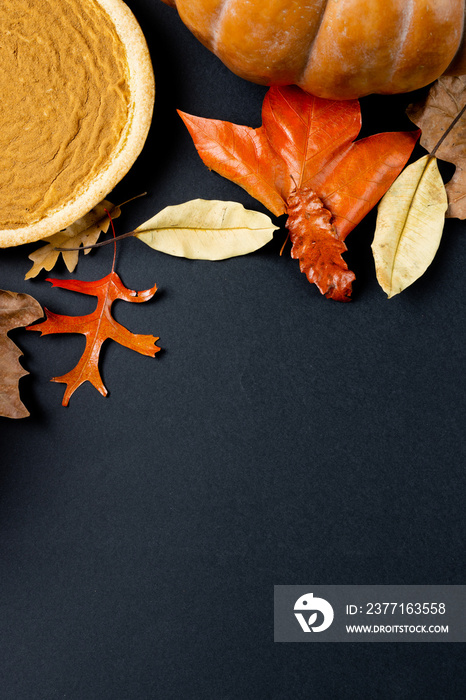 Composition of pumpkin, colorful autumn leaves and pie on black background